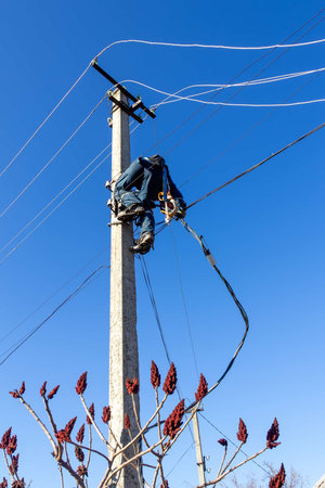 a male electrician climbs up a reinforced concrete pole to install a line of electrical wires