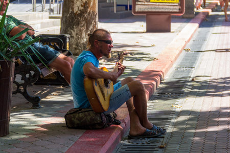 Kerch, Russia - 13 August 2019: a street musician plays guitar and sings while sitting on the...