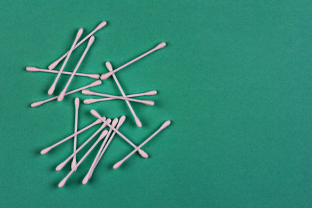 cotton swabs are scattered on a green background close up view from above with a copy space