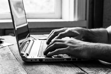 hands of a man working at a computer laptop at the window, black and white photoの写真素材