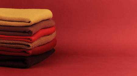 Stack of colorful folded sweaters on brown maroon background with copy spaceの写真素材