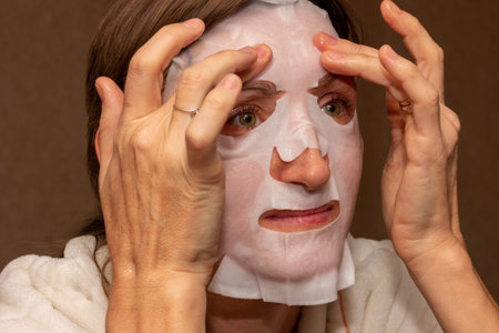 a young woman puts a white moisturizing mask on her face