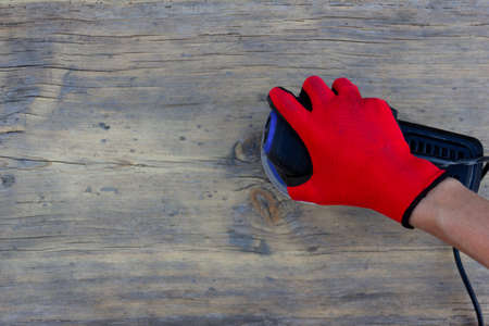 female hand in a red protective glove is grinding an old gray board with an electric sander, top view with copy spaceの写真素材