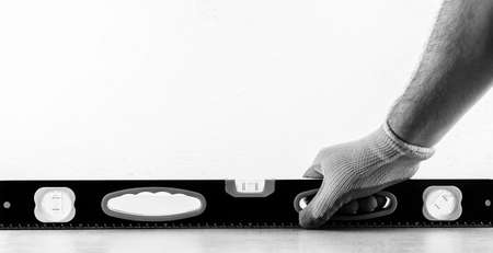 a male construction worker checks the construction level of a ceramic tile floor covering against a white wall with a copy space, black and white photoの写真素材