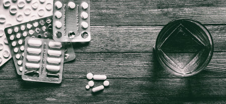glass of water pills and capsules on wooden table top view, monochrome photoの写真素材