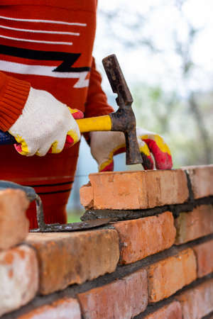 a man builds a brick wall, puts a brick on a cement-sand mortar, tapping a brick with a hammerの写真素材