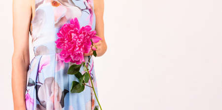 a young woman in a colorful dress with a peony flower in her hand on a light pink background with a copy spaceの写真素材