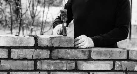 a man builds a wall of bricks, lays a brick on a cement-sand mortar, tapping a brick with a hammer, black and white photoの写真素材