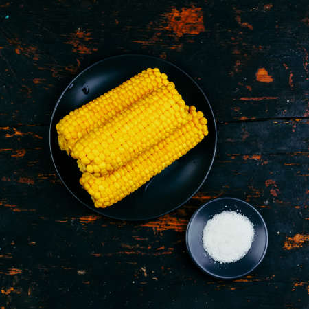 cobs of boiled corn and salt on a black plate on a wooden vintage black table top viewの写真素材