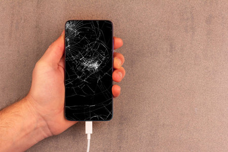 smartphone with broken screen in male hand on gray-brown background with copy space