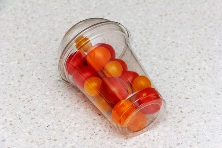 small red and yellow tomatoes in a plastic transparent glass are lying on the table close-up