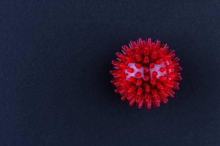 red medical massager in the form of a ball with spikes on a gray background with a copy space
