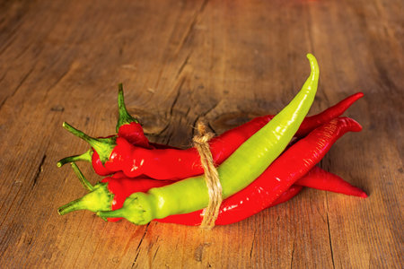a bunch of red and green hot pepper tied with twine on an old wooden background close-up