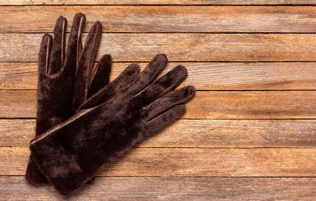a pair of warm women's fur gloves on a wooden background, top view with copy spaceの写真素材