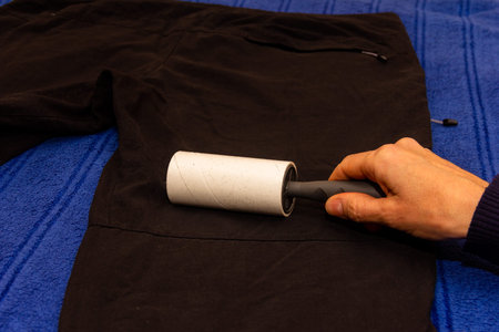 female hand with sticky roller for cleaning clothes cleans black mens trousers close-up
