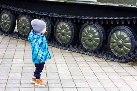a little boy stands and looks at a large military self-propelled installation on a caterpillar trackの写真素材