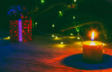 a red Christmas box with a gift and a burning candle on the background of a natural fir tree with Christmas lightsの写真素材