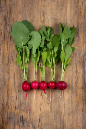 ripe red radish with green leaves on a wooden background top view