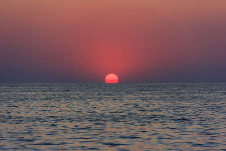 beautiful sunset with the red sun hiding behind the horizon in the seaの写真素材