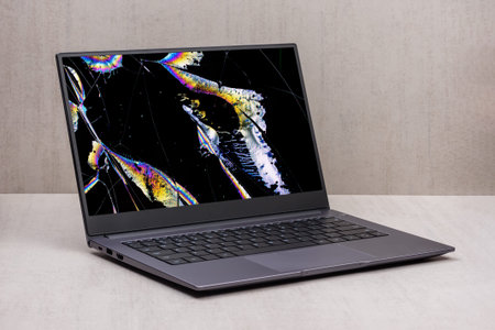 laptop with a broken screen in color spots and cracks on a gray background close up