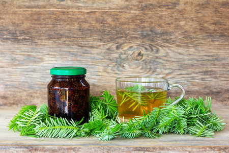 a drink made of pine needles in a cup with green fir needles and jar pine cone jam on a wooden background with a close-up copy spaceの写真素材