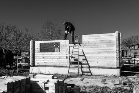 a man builds a house made of profiled timber in the countryside against the blue sky, black and white photoの写真素材