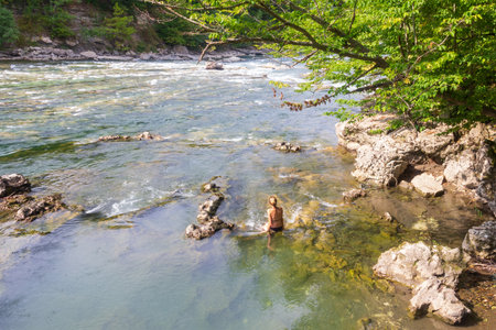 a young woman, a girl is sitting in the water of a mountain river on a hot summer dayの写真素材