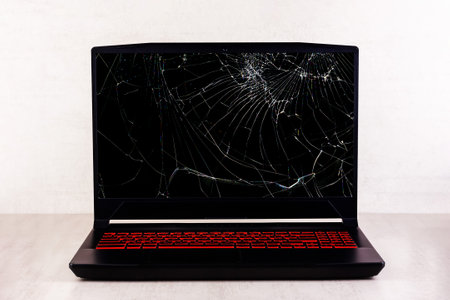 a gaming laptop with a broken screen in cracks on a gray background close up front viewの写真素材