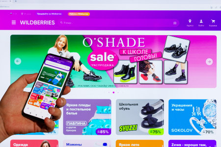 Adygea, Russia - August 09, 2023: hand man with smartphone making purchases in Wildberries online store in mobile application against background Wildberries marketplace web page open computer monitorのeditorial素材