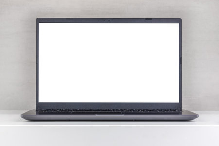 white mock-up on a laptop screen on a white table against a gray wall close-up front viewの写真素材
