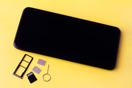 smartphone and open slots for nano SIM cards, two nano SIM cards, micro SD drive and metal key on yellow backgroundの写真素材