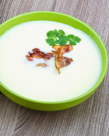 A close-up of a bowl of smooth, white soup, artfully garnished with fresh green herbs and crispy fried elements.の写真素材
