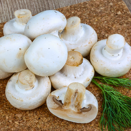 A pile of fresh white button mushrooms, some whole and one cut in half, with a sprig of dill on a textured burlap surface.の写真素材