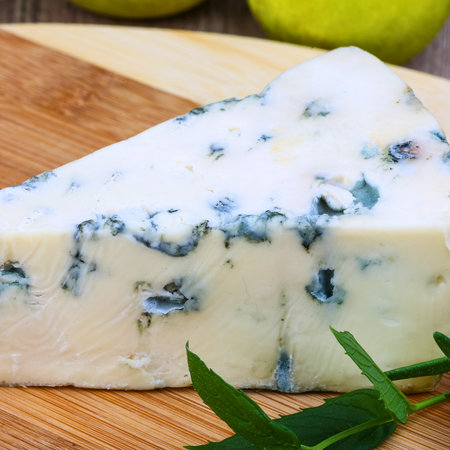 A detailed view of a triangular slice of blue cheese, showcasing its creamy texture and distinctive blue-green mold veins.の写真素材