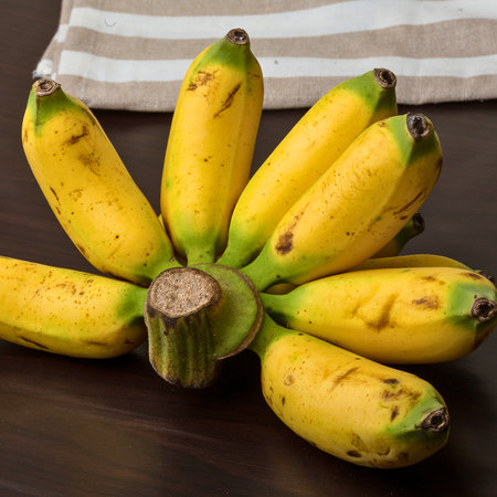 A close-up shot showcases a cluster of bright yellow bananas with hints of green at the stems, resting on a dark, textured surface.の写真素材