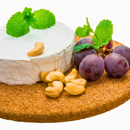 A delicious cheese board featuring brie, cashews, fresh plums, and mint leaves, presented on a cork base.の写真素材