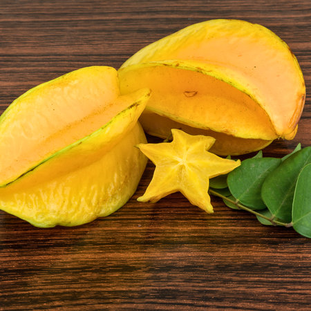 Two whole star fruits and one sliced star fruit with green leaves on a dark wooden background.の写真素材