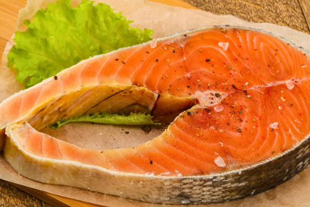 A close-up, overhead view of a perfectly cooked salmon steak seasoned with salt and pepper, served with a vibrant green lettuce leaf.の写真素材