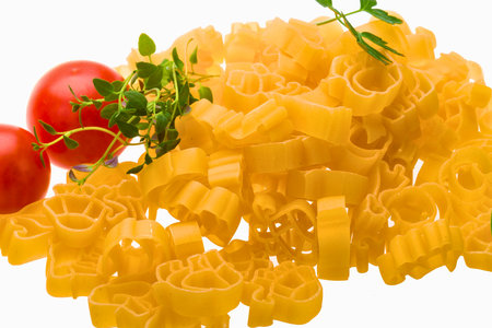 A close-up shot of golden ring-shaped pasta, garnished with bright red tomatoes and fresh green herbs, isolated on a white background.の写真素材
