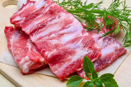 Close-up of uncooked pork ribs with marbled fat, garnished with fresh dill and basil, on a wooden surface.の写真素材