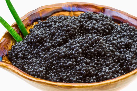 A close-up of glistening black caviar piled high in a decorative bowl, garnished with vibrant green chives, suggesting a gourmet culinary experience.の写真素材