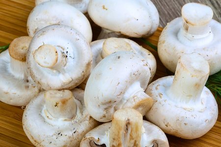 A close-up overhead view of a pile of fresh, white button mushrooms resting on a textured wooden surface.の写真素材