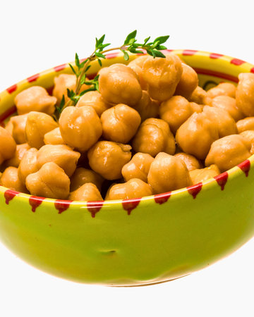 A vibrant bowl overflowing with golden brown chickpeas, garnished with fresh green herbs, presented against a white background.の写真素材