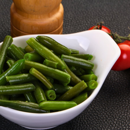 A close-up shot of vibrant green beans, lightly cooked and served in a white bowl, with ripe red tomatoes in the background.の写真素材