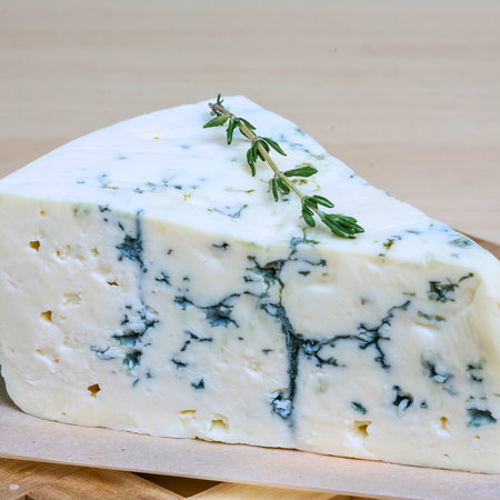 A detailed view of a creamy blue cheese wedge, showcasing its characteristic blue veins and a fresh sprig of thyme on top.の写真素材
