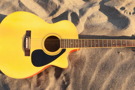 Acoustic guitar with a bright yellow body rests on a textured surface with natural wood grain patterns.の写真素材