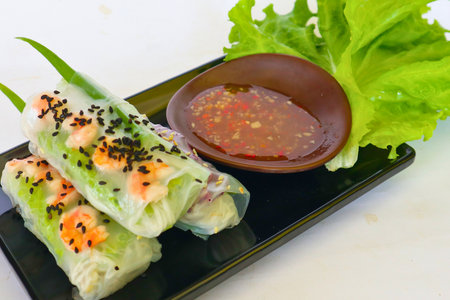 Three translucent summer rolls filled with shrimp and vegetables, served with a savory dipping sauce and a crisp lettuce leaf.の写真素材