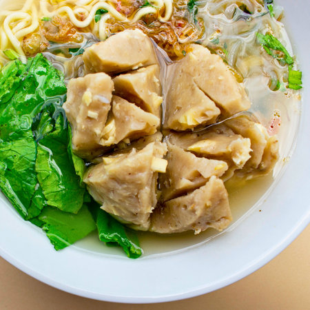 A close-up shot of a large, savory meatball served in a flavorful broth with noodles, vegetables, and clear noodles.の写真素材