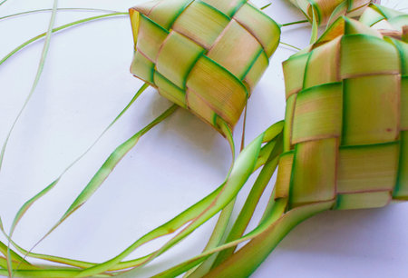 Close-up view of intricately woven ketupat, a Southeast Asian rice cake, made from palm leaves on a white surface.の写真素材