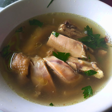 A close-up shot of a bowl filled with savory chicken soup, featuring chunks of tender chicken and fresh green herbs.の写真素材